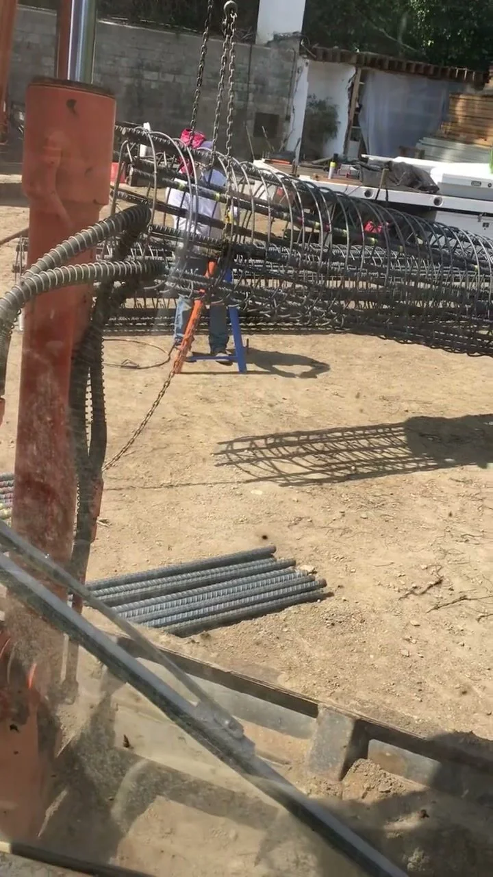 A Sierra Development crew member guiding a large cylindrical rebar cage into position for a retaining wall footing.